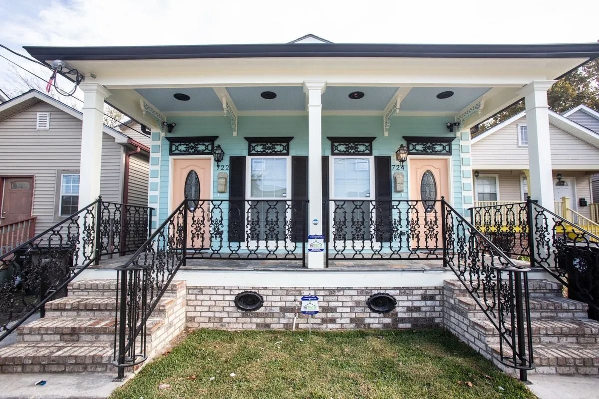 Two-unit residential building with a shared porch and matching doors, light blue facade, and black wrought iron.