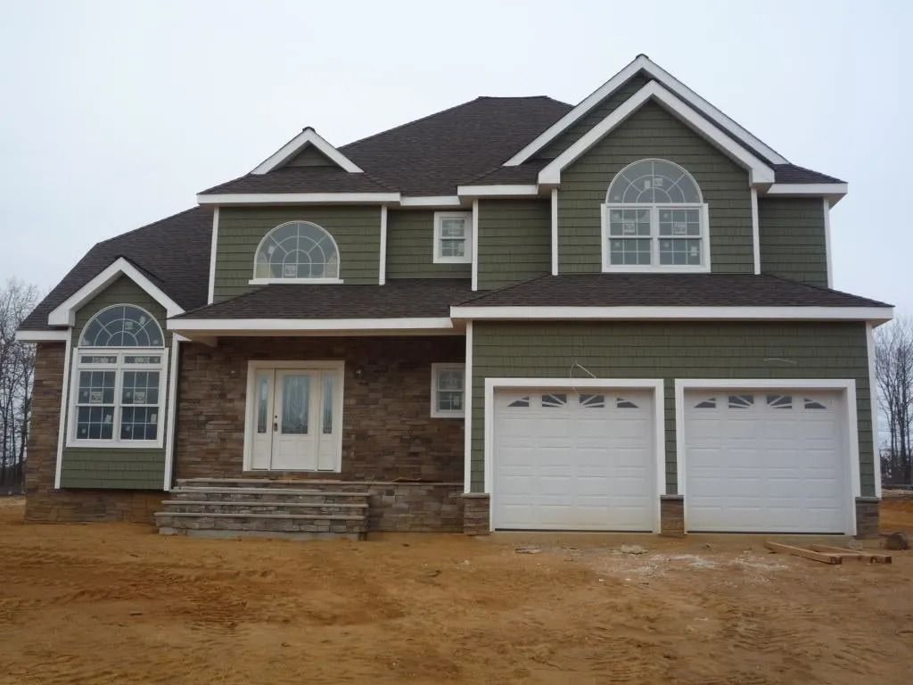 Two-story house with green siding, brown brick base, and white garage doors under a dark roof.
