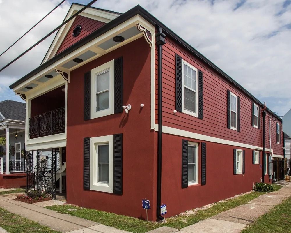 Red two-story building with black shutters, white window frames, and decorative trim, on a sidewalk with grass.