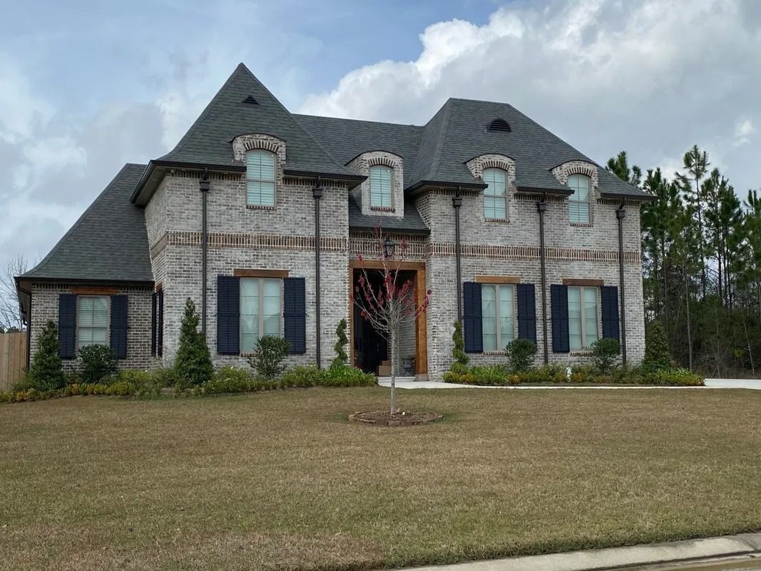 Two-story brick house with dark roof and shutters, windows, and manicured lawn.