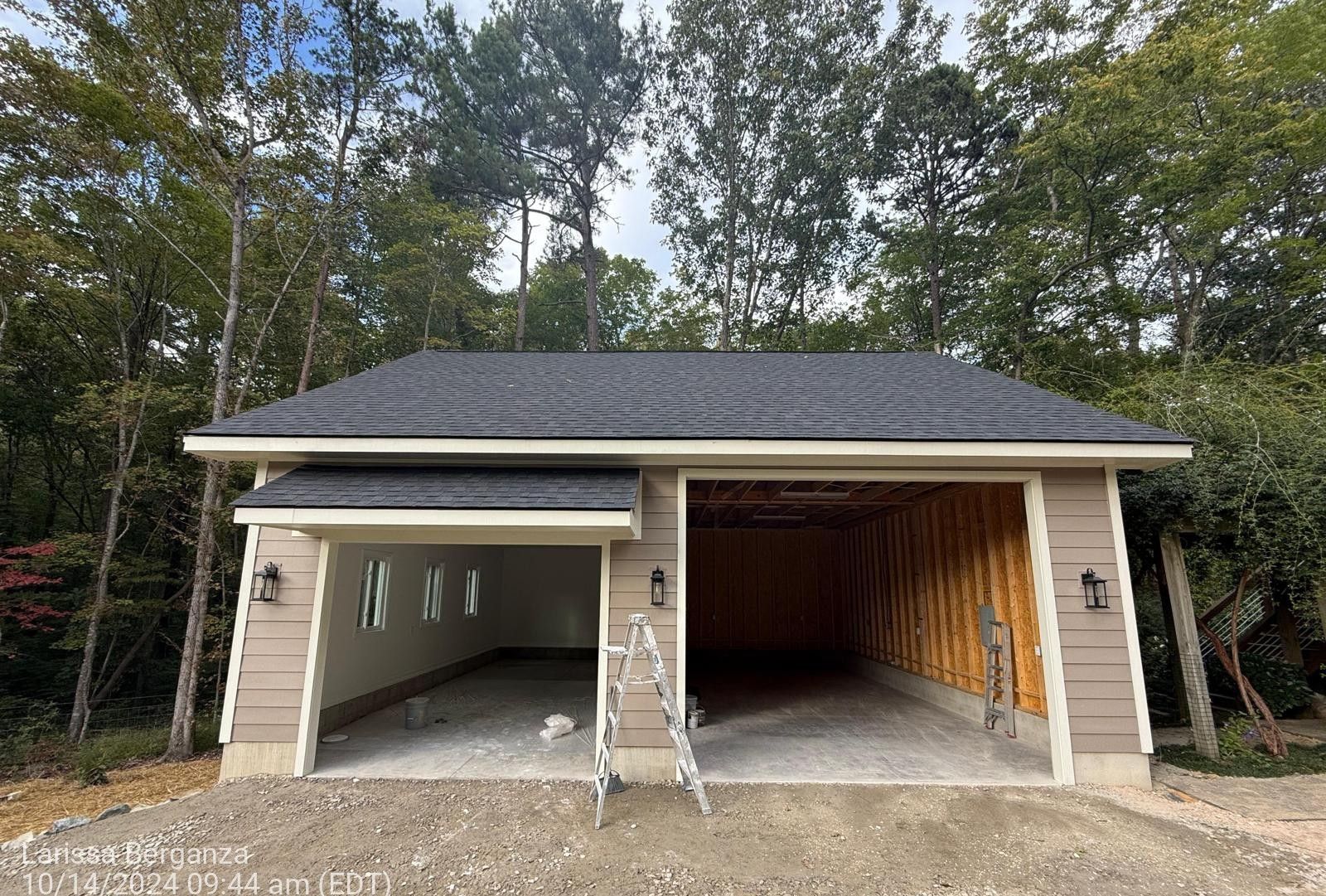 A garage with a black roof is being built in the woods.