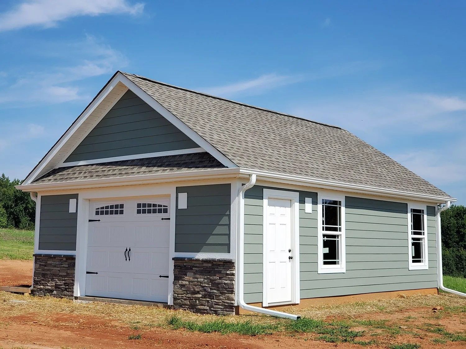 A small house with a garage and a roof is sitting in the middle of a field.