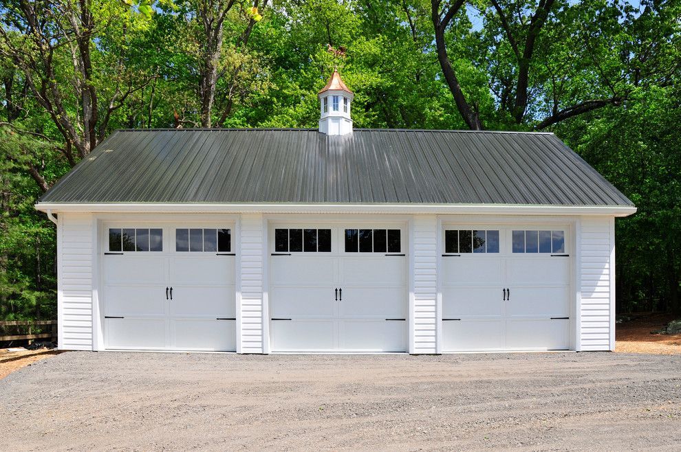 A white garage with a black roof is surrounded by trees
