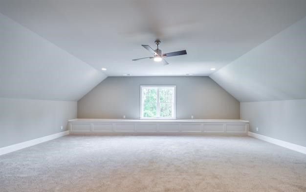An empty attic with a ceiling fan and a window.