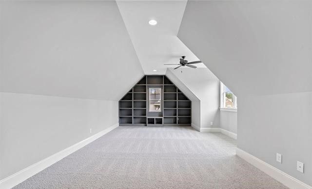 An empty attic with a ceiling fan and shelves.