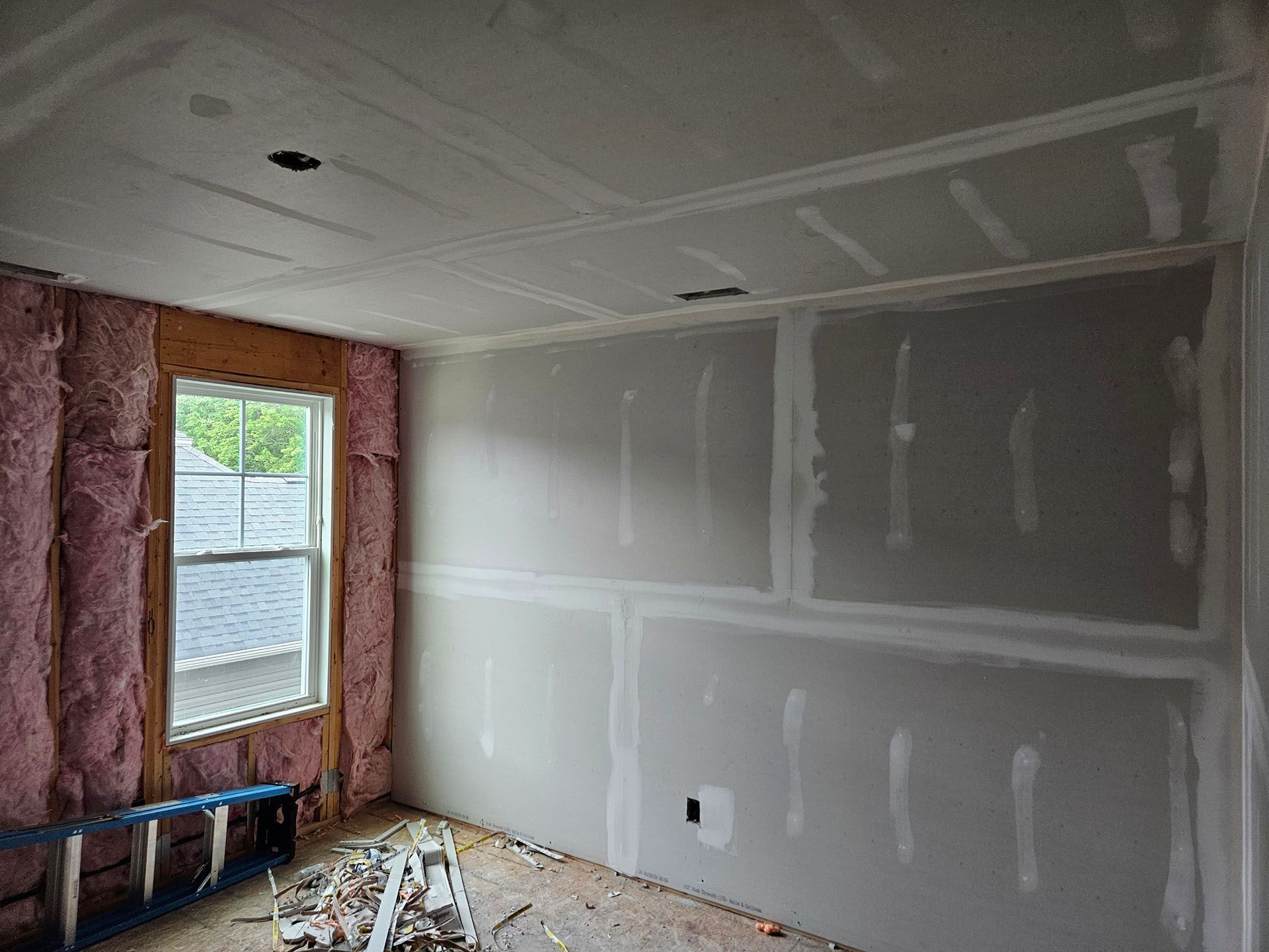 A room with a window and a ladder in it is being remodeled.