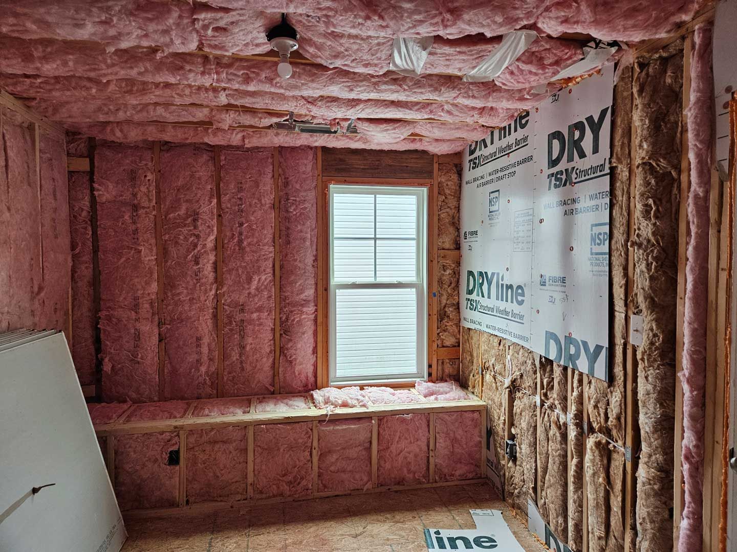 A room with pink insulation and a window.