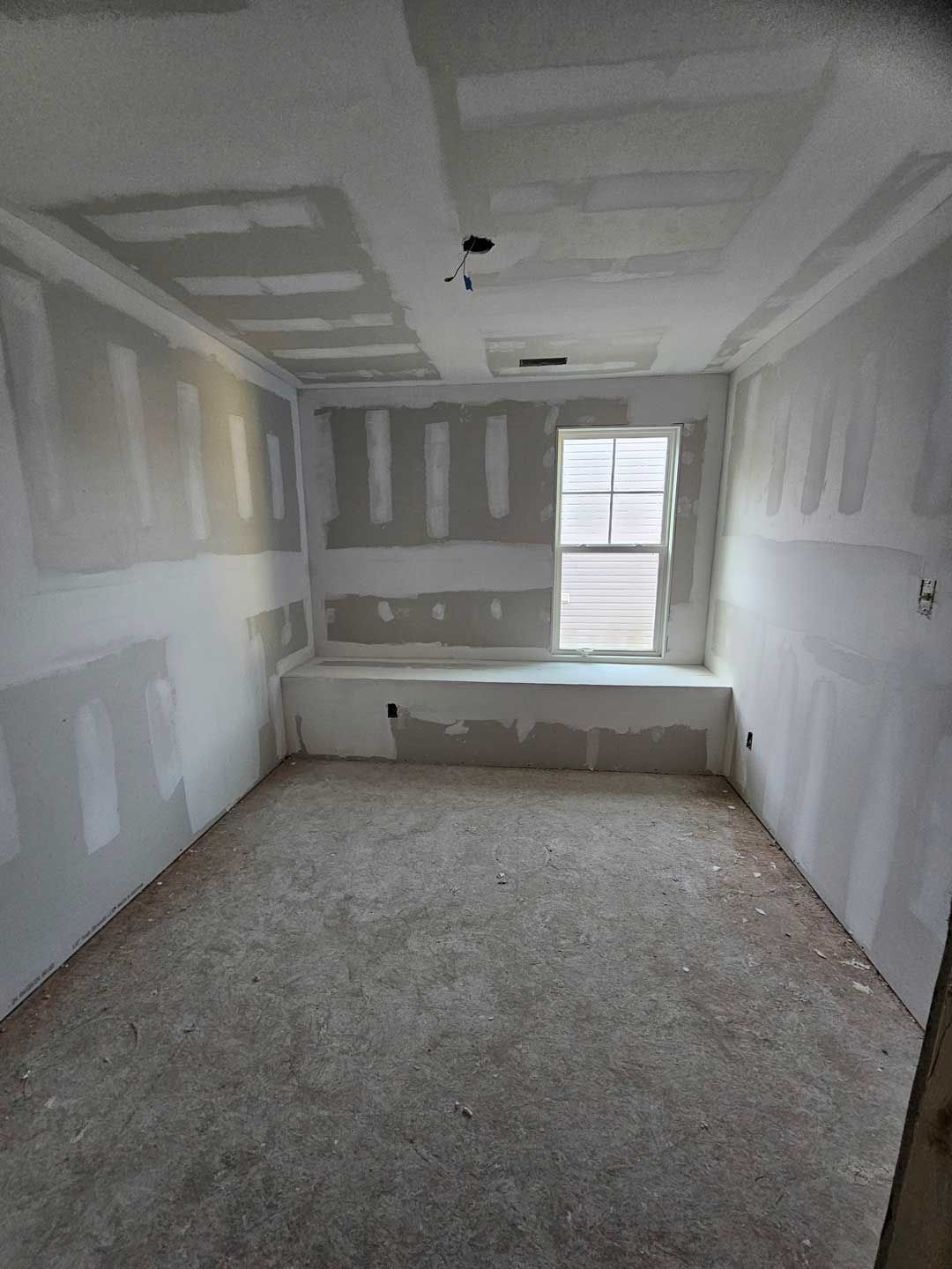An empty room with drywall on the walls and a window.