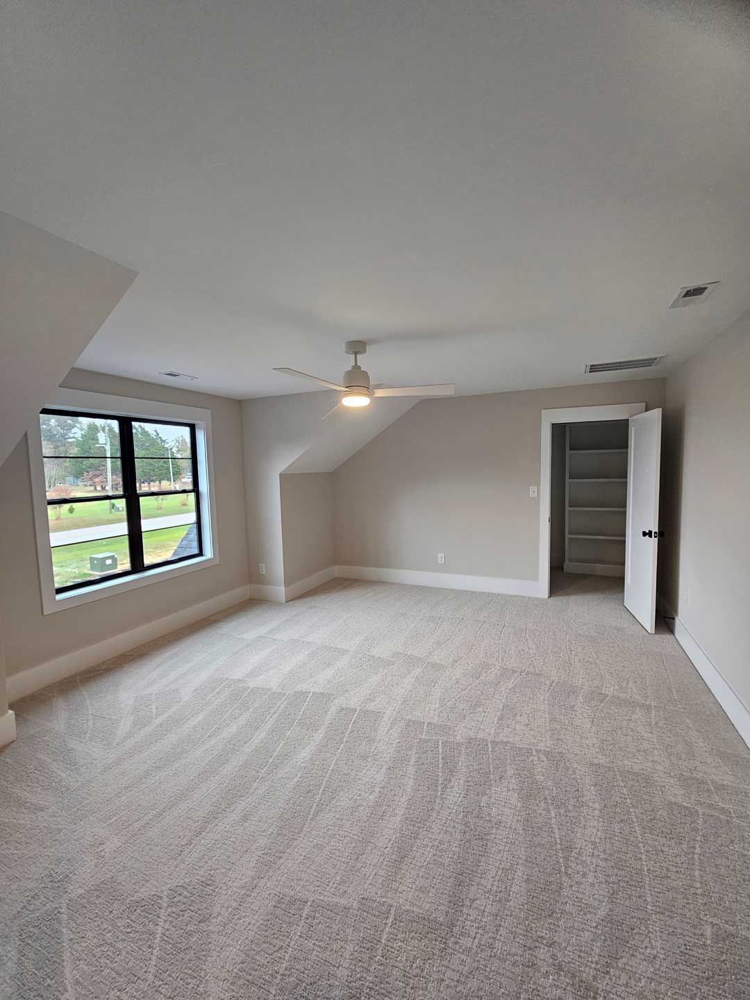 An empty bedroom with a ceiling fan and a window.