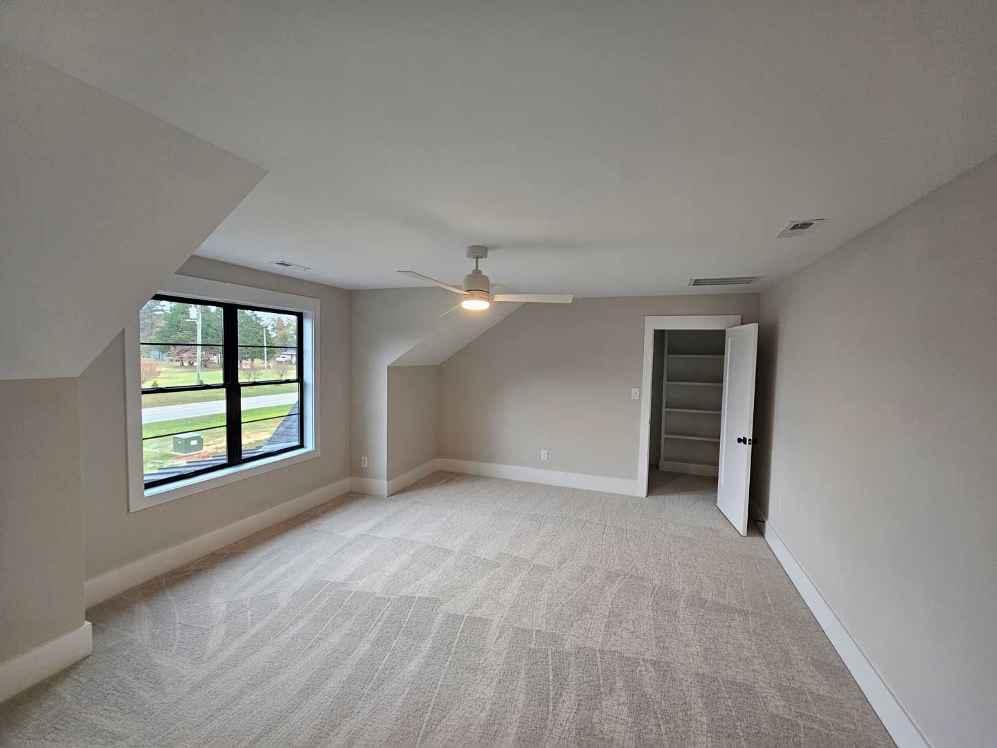 An empty bedroom with a ceiling fan and a window.