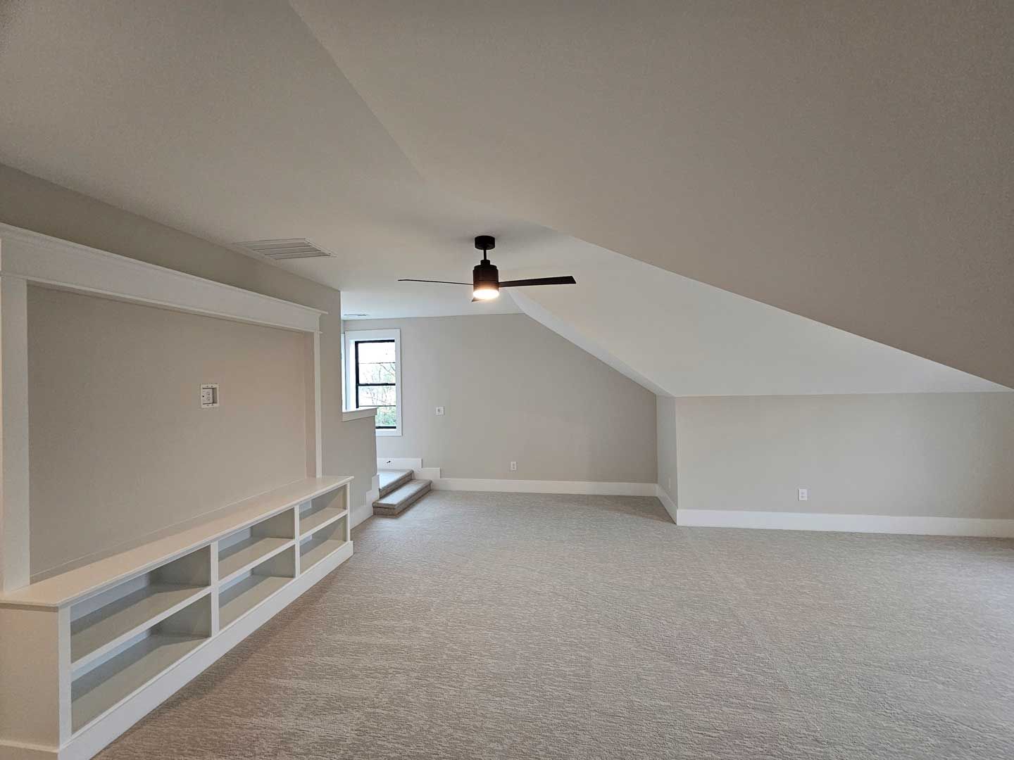 An empty room with a ceiling fan and shelves.