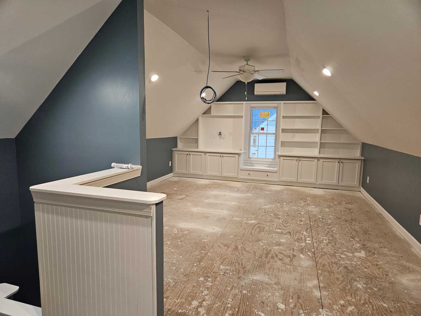 An empty attic with a ceiling fan and shelves.