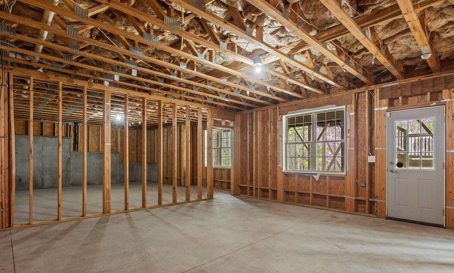 An empty room in a house under construction with wooden beams and windows.