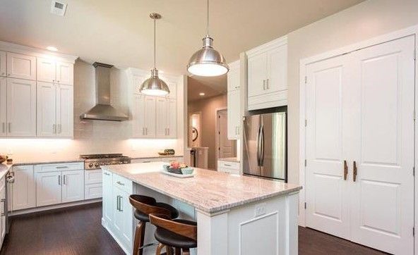 A kitchen with white cabinets , granite counter tops , stainless steel appliances and a large island.