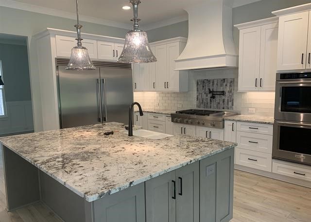 A kitchen with white cabinets , granite counter tops , stainless steel appliances and a large island.