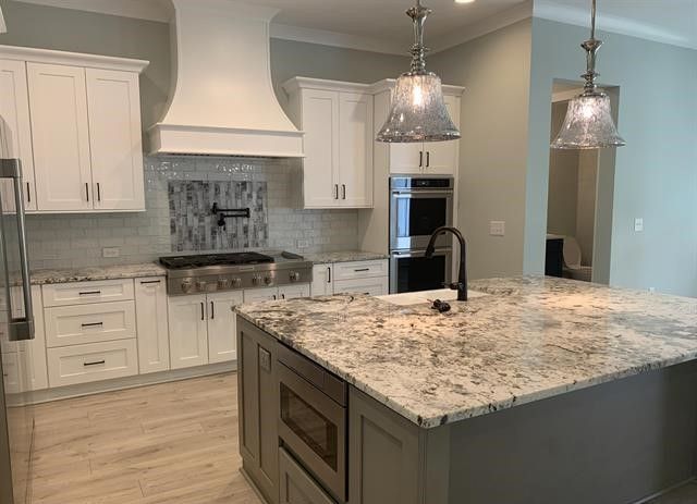 A kitchen with white cabinets , granite counter tops , stainless steel appliances and a large island.