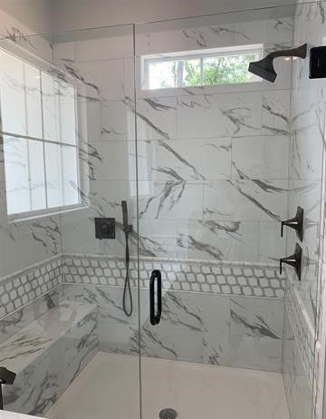 A bathroom with marble tiles and a walk in shower with a glass door.