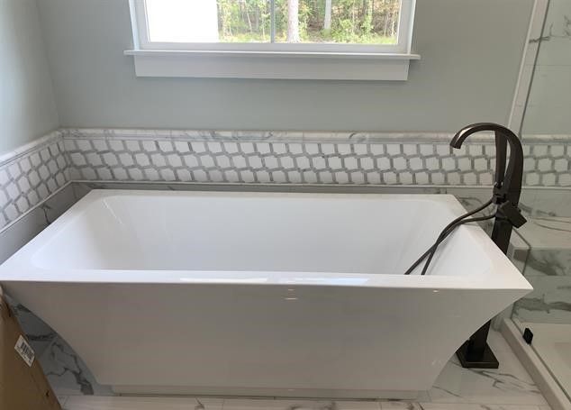 A white bathtub is sitting in a bathroom next to a window.