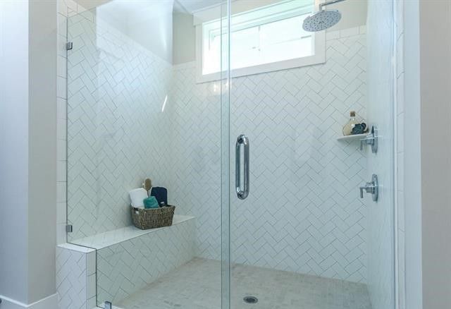A bathroom with a walk in shower with a glass door and a window.