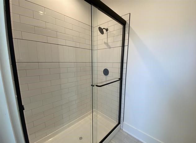 There is a shower with a black frame and white tiles.