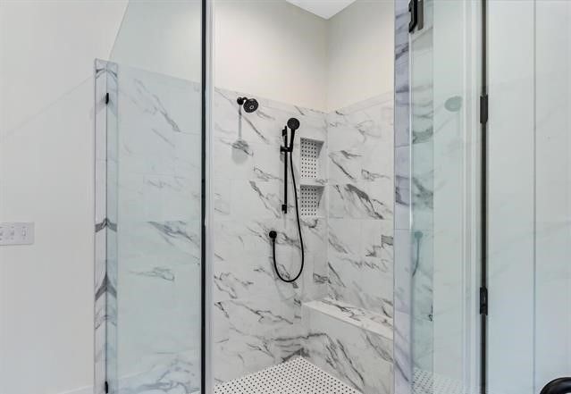 A bathroom with a walk in shower with marble walls and a glass door.