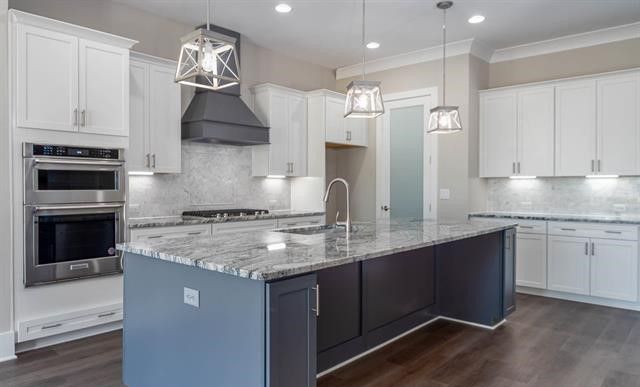 A kitchen with white cabinets , granite counter tops , stainless steel appliances and a large island.