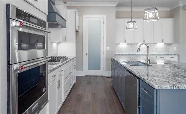 A kitchen with white cabinets , stainless steel appliances , granite counter tops and a large island.