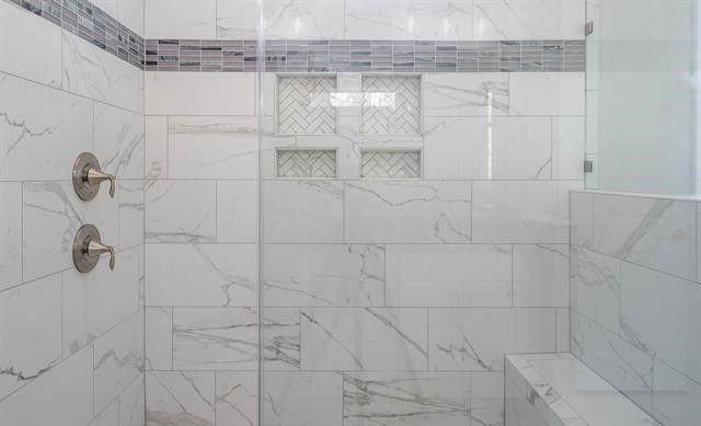 A bathroom with marble tiles and a walk in shower with a glass door.