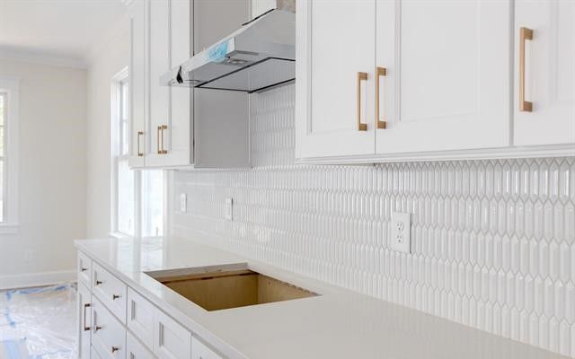 A kitchen with white cabinets , a sink , and a hood.
