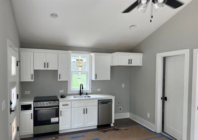 A kitchen with white cabinets , a stove , a sink , and a ceiling fan.
