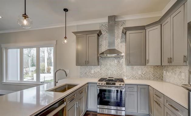 A kitchen with gray cabinets , stainless steel appliances , a sink , and a stove.