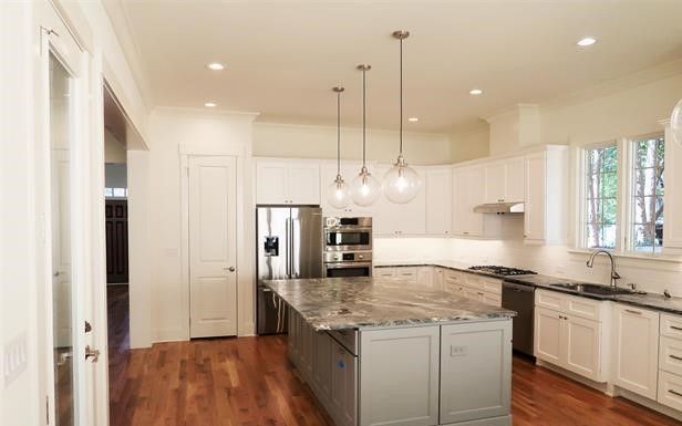 A kitchen with white cabinets , granite counter tops , stainless steel appliances and a large island.