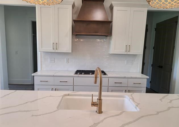 A kitchen with white cabinets , a sink , a stove and a hood.