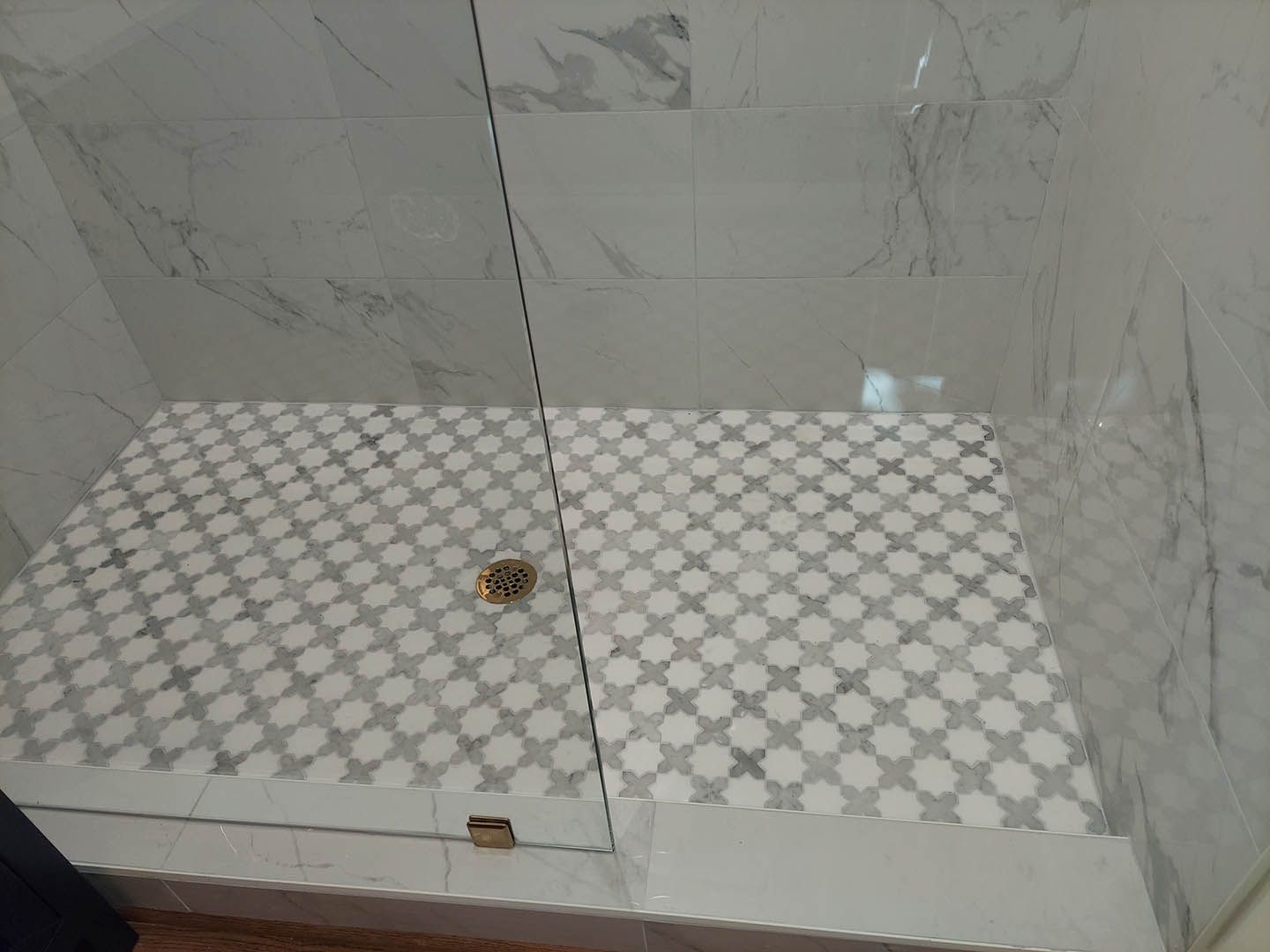 A walk in shower with a tiled floor and a glass door.