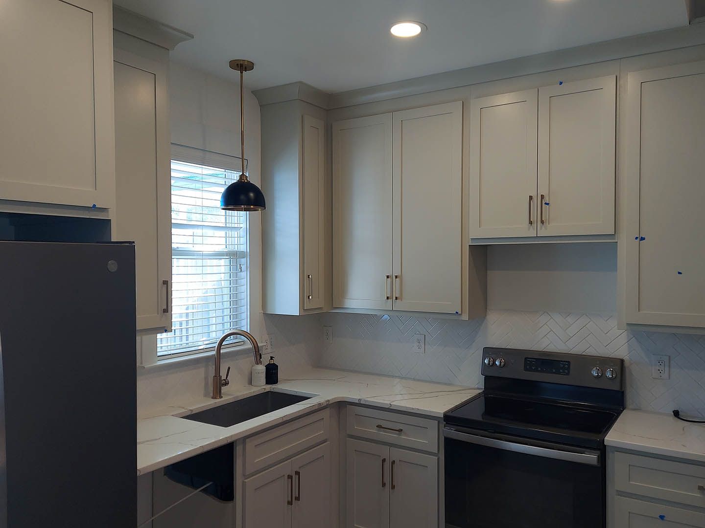 A kitchen with white cabinets , a stove , a sink , and a refrigerator.