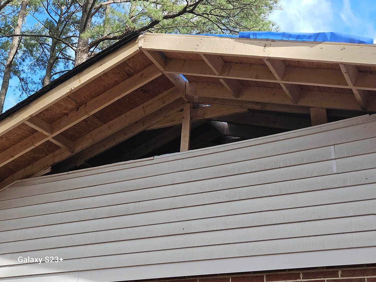 The roof of a house is being built with a blue tarp on top of it.