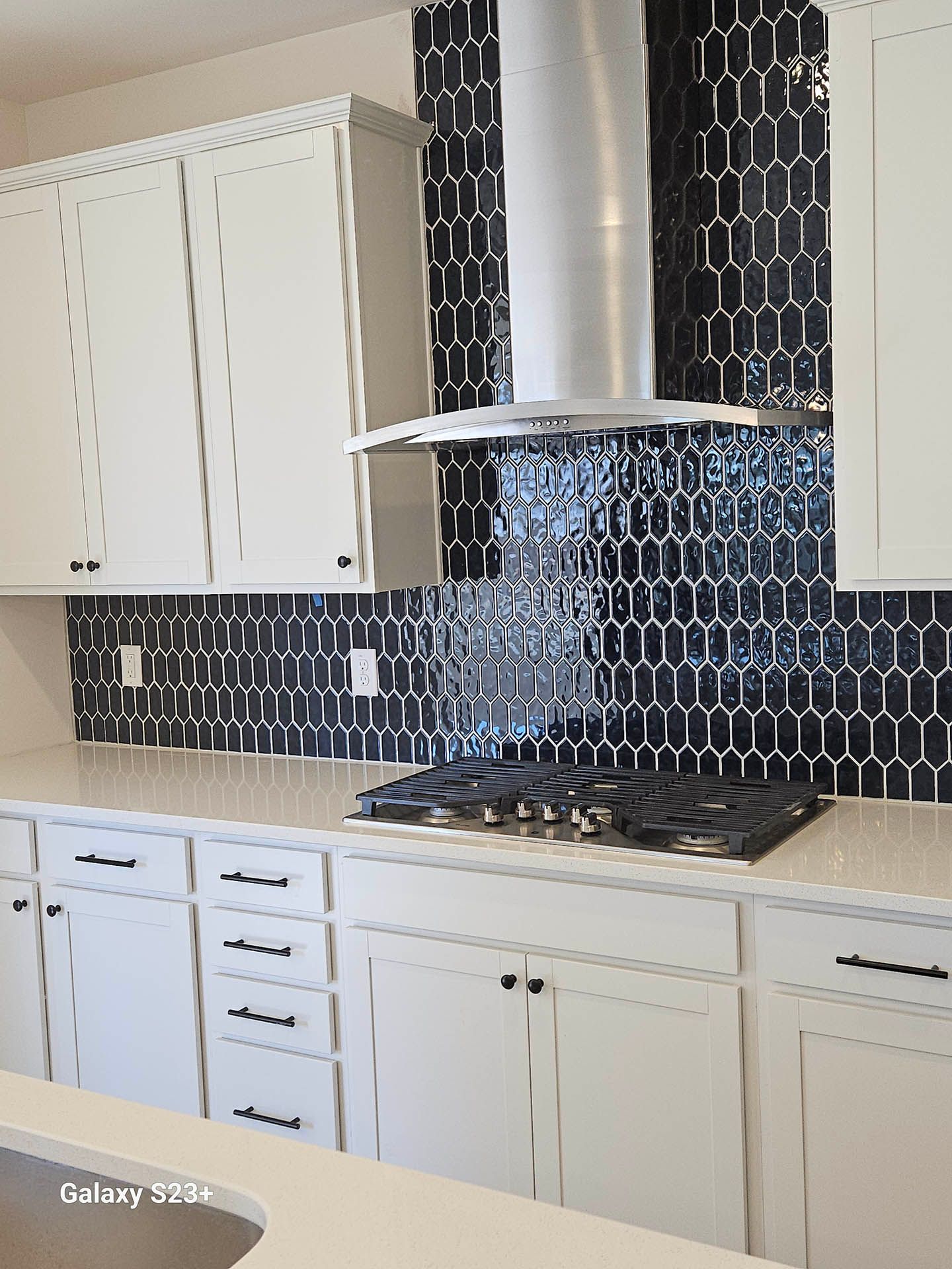 A kitchen with white cabinets and black tiles and a stove top oven.