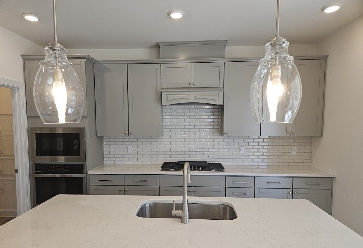 A kitchen with gray cabinets , a sink , a stove and a microwave.