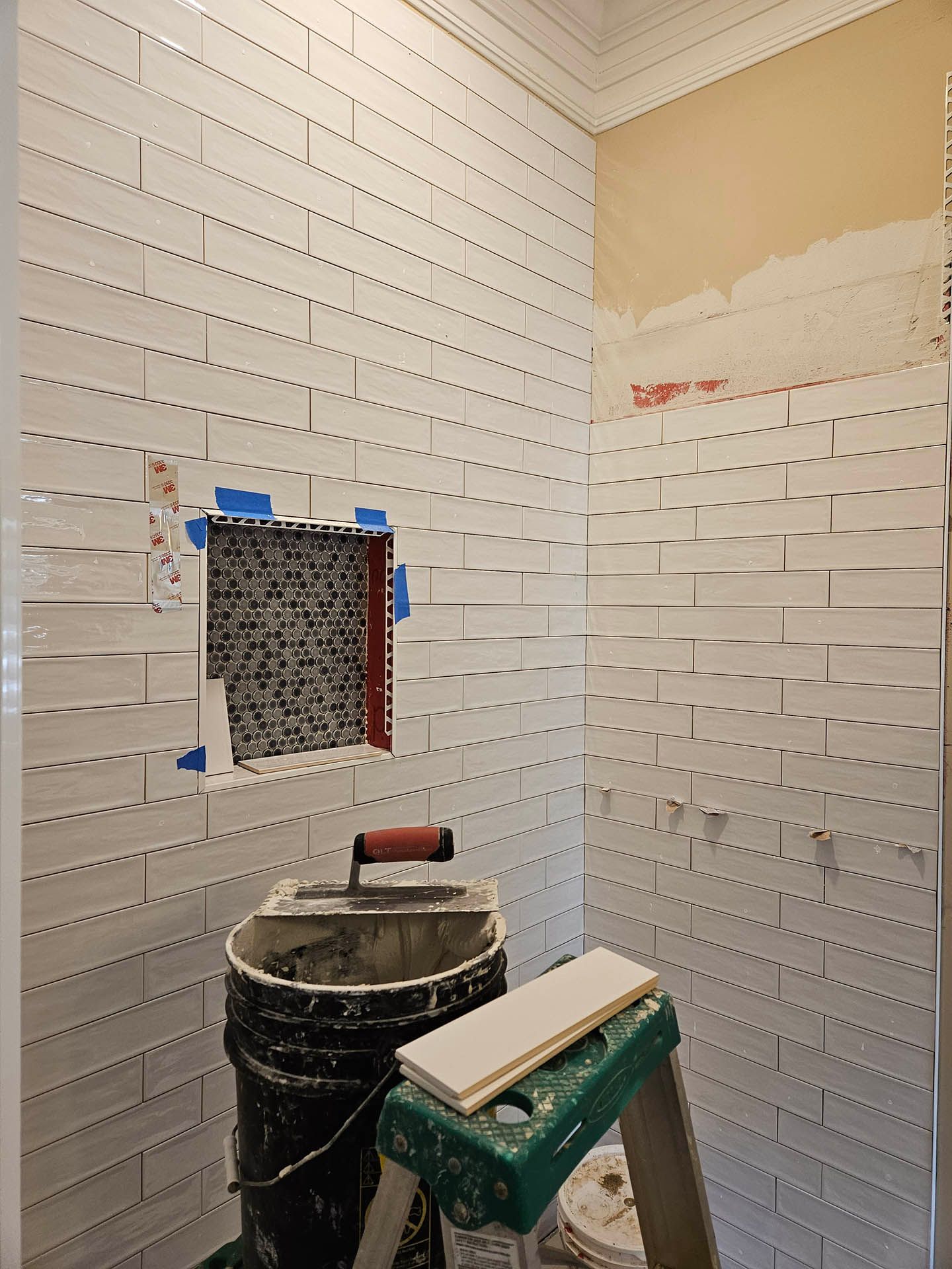 A bathroom with white tiles being installed and a ladder.