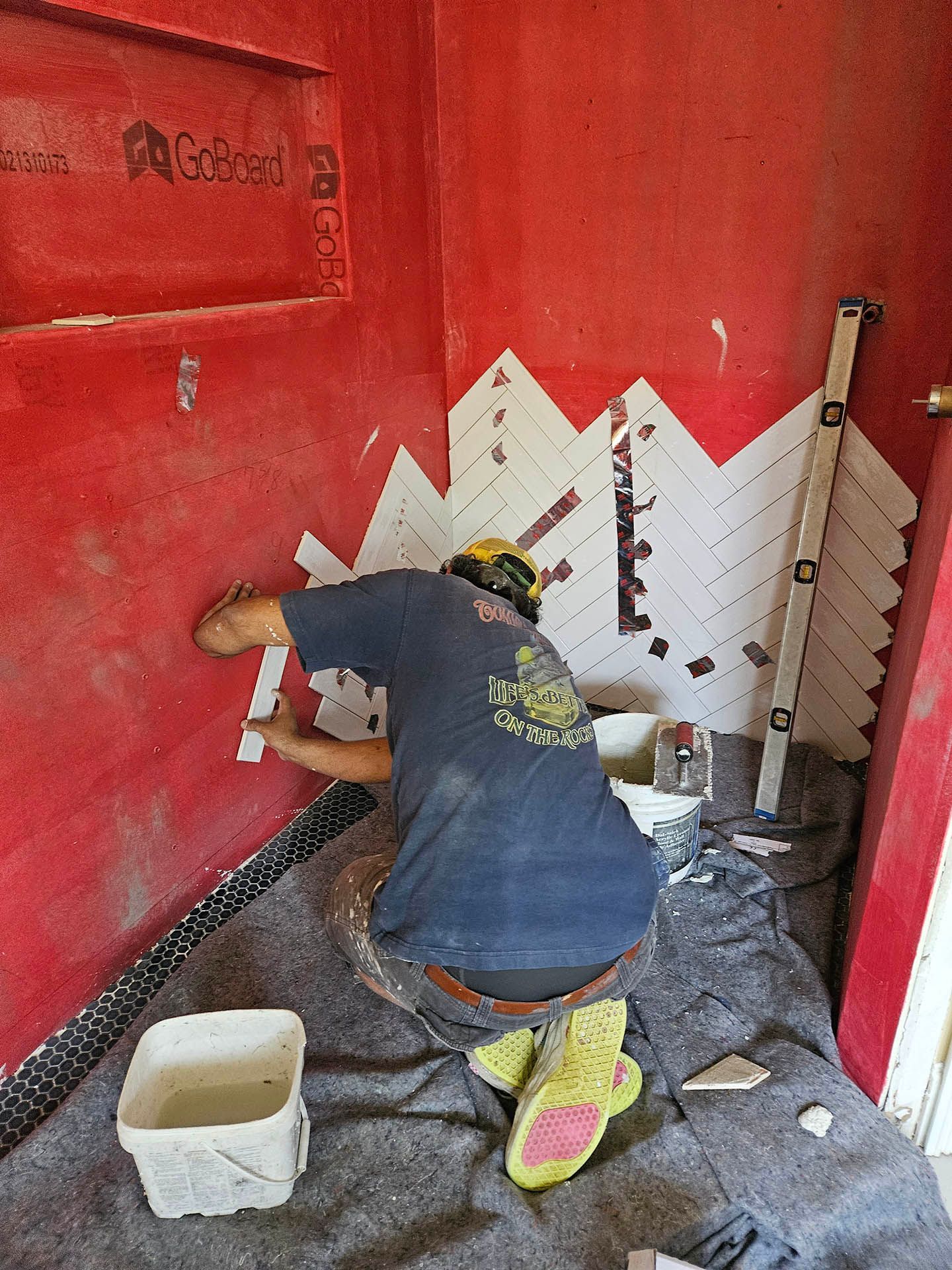 A man is kneeling down in front of a red wall.