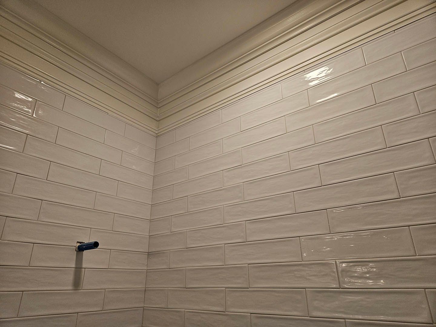 A bathroom with white tiles and a shower head.