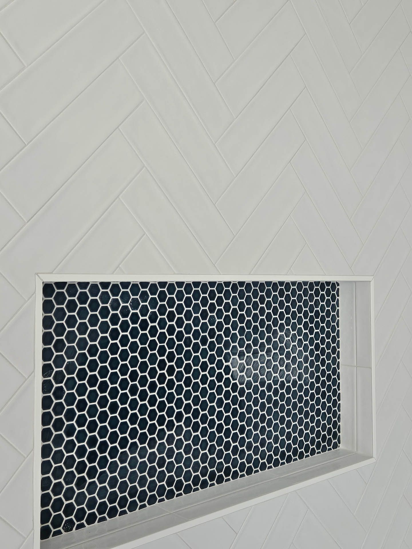 A shower niche with black and white tiles on a white wall.