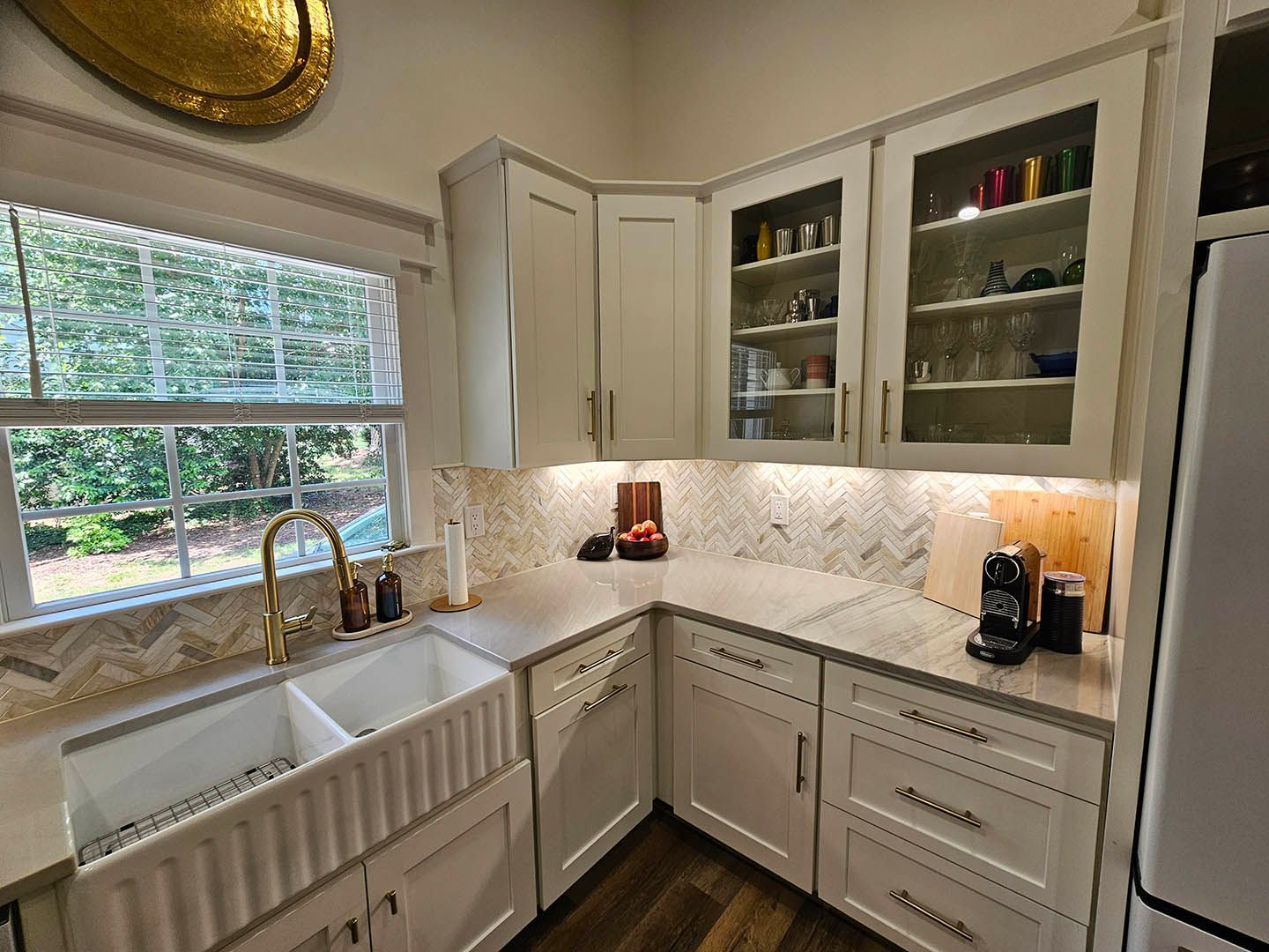 A kitchen with white cabinets , a sink , a refrigerator , and a window.