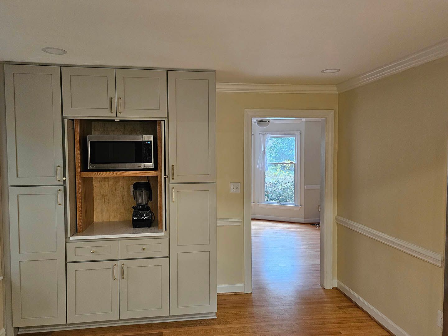 A kitchen with white cabinets , a microwave , and a blender.