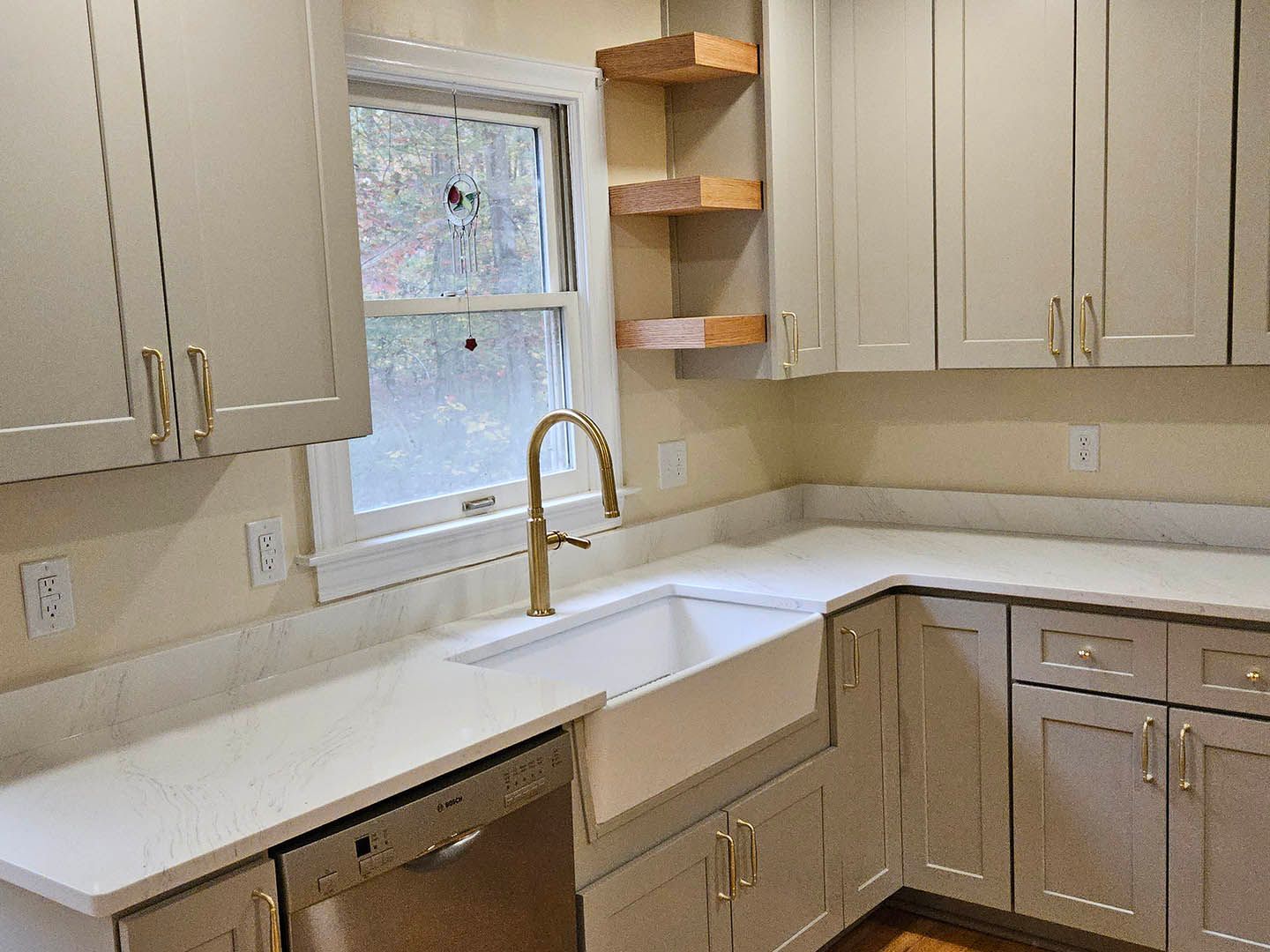 A kitchen with white cabinets , a sink , a dishwasher , and a window.