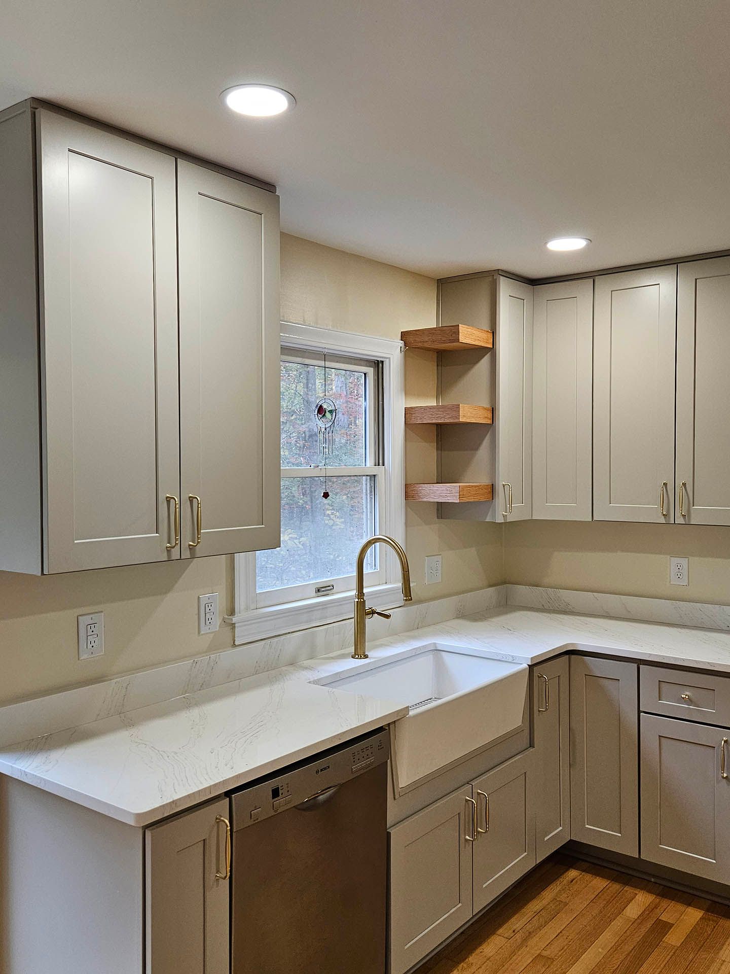 A kitchen with white cabinets , a sink , a dishwasher , and a window.