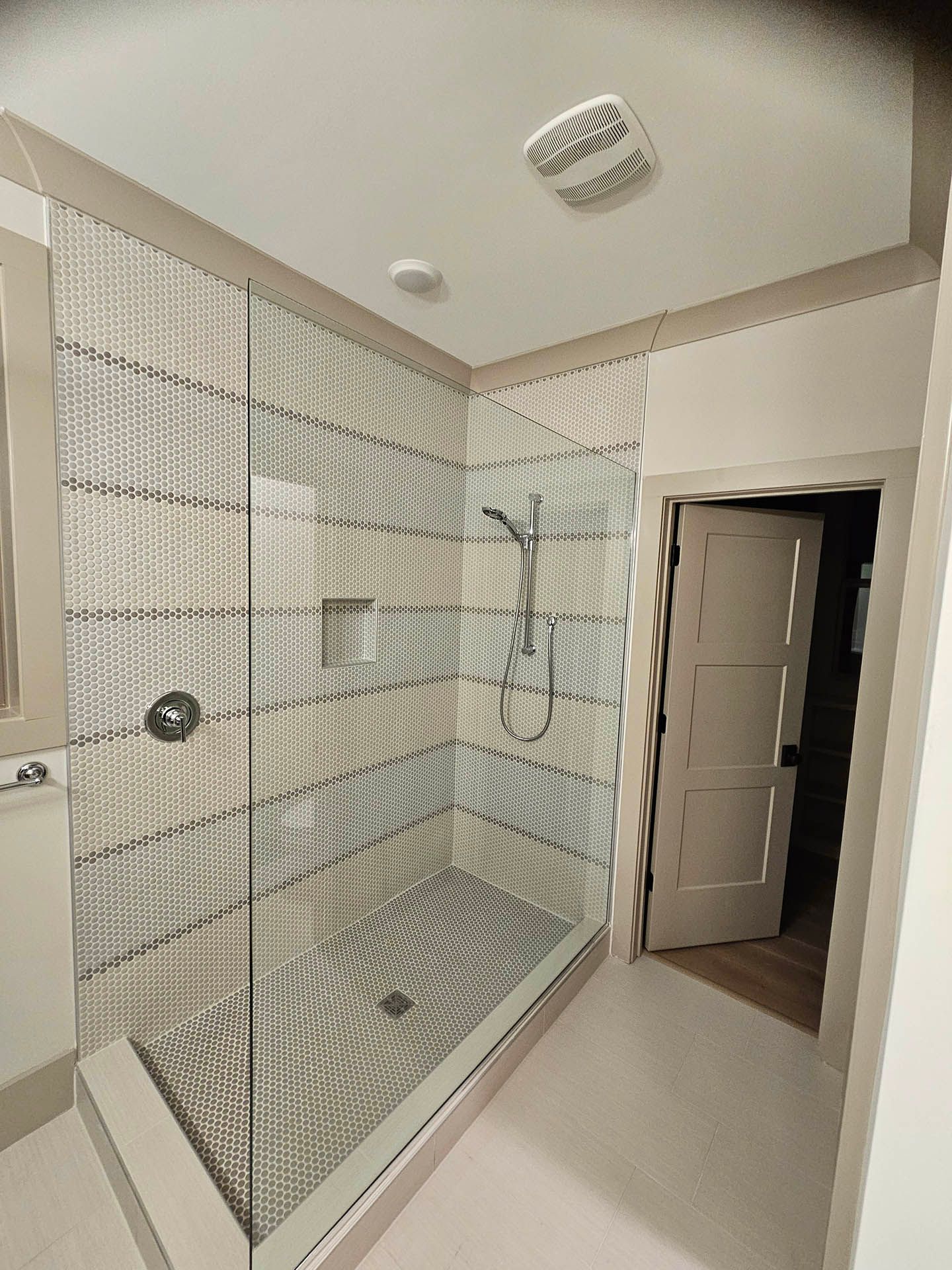 A bathroom with a walk in shower and a door leading to a closet.