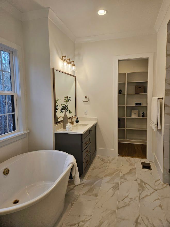 A bathroom with a tub , sink , mirror and walk in closet.