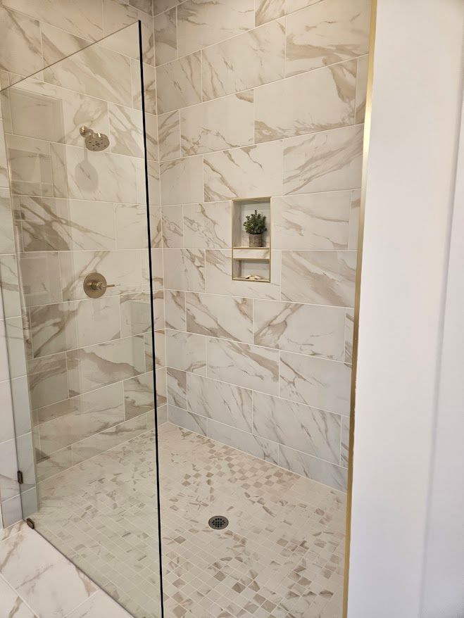 A walk in shower with marble tiles and a glass door.