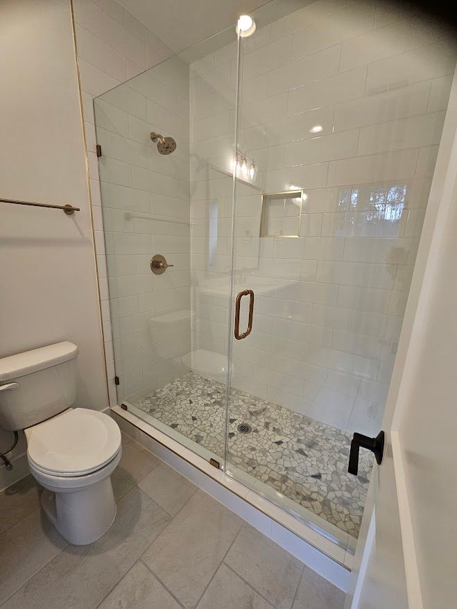 A bathroom with a toilet and a walk in shower with a glass door.